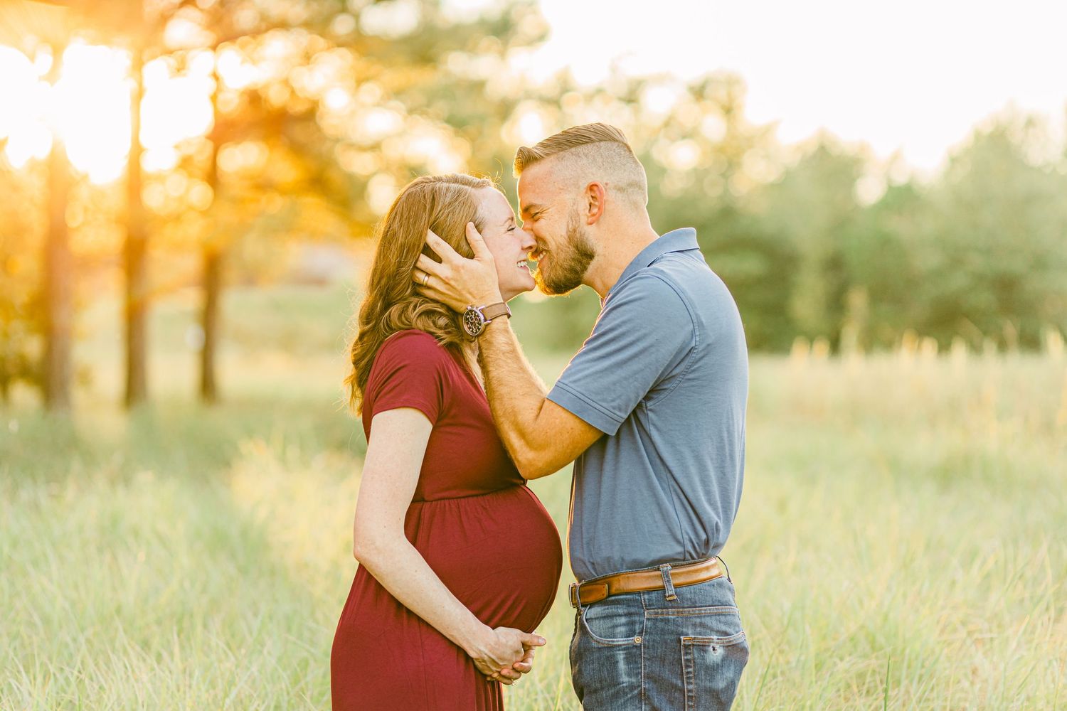 a husband holds his pregnant wife's face in his hands as he leans in for a kiss