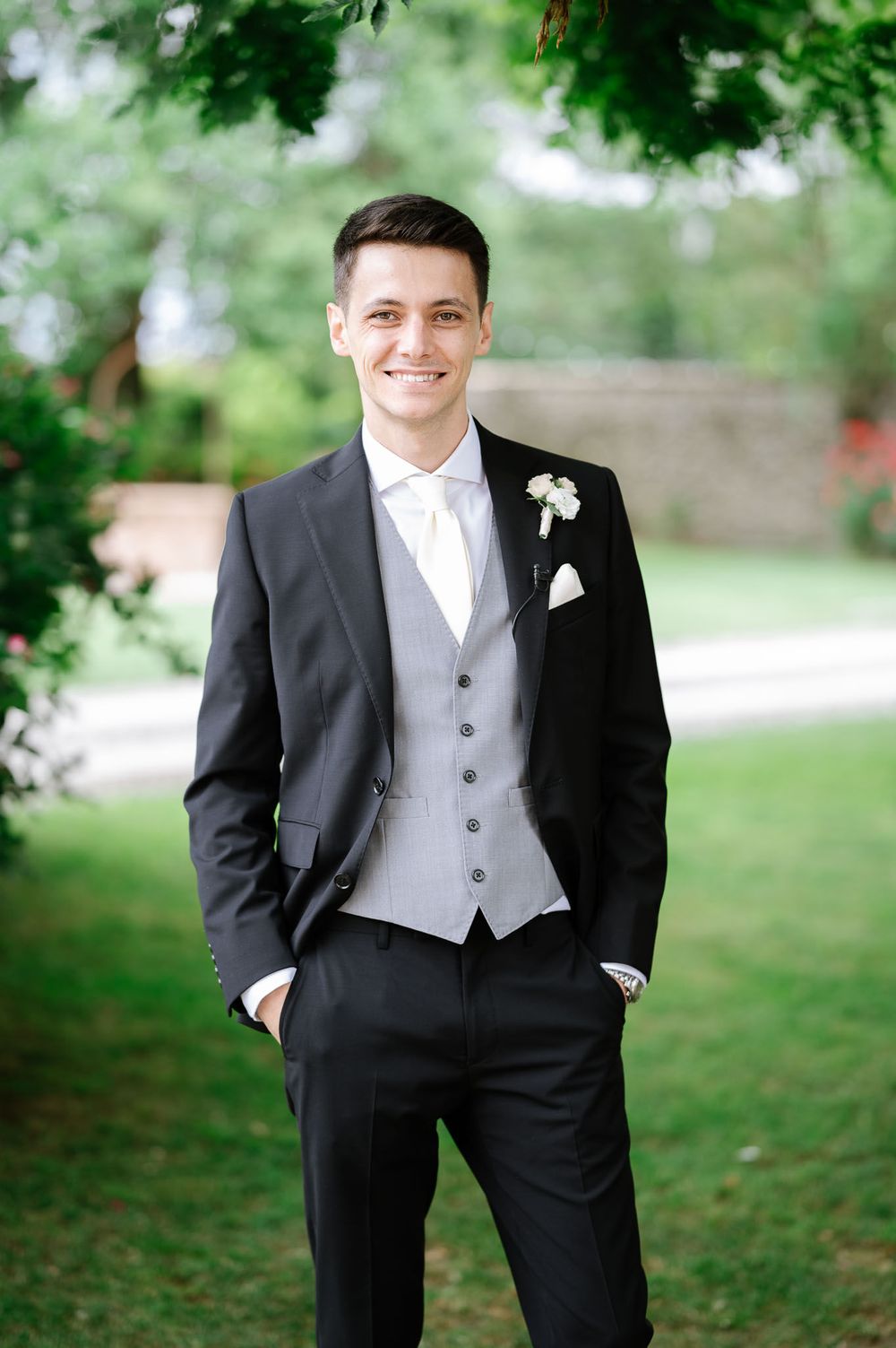 A formal black tuxedo with gray vest and white boutonniere is worn for a wedding.