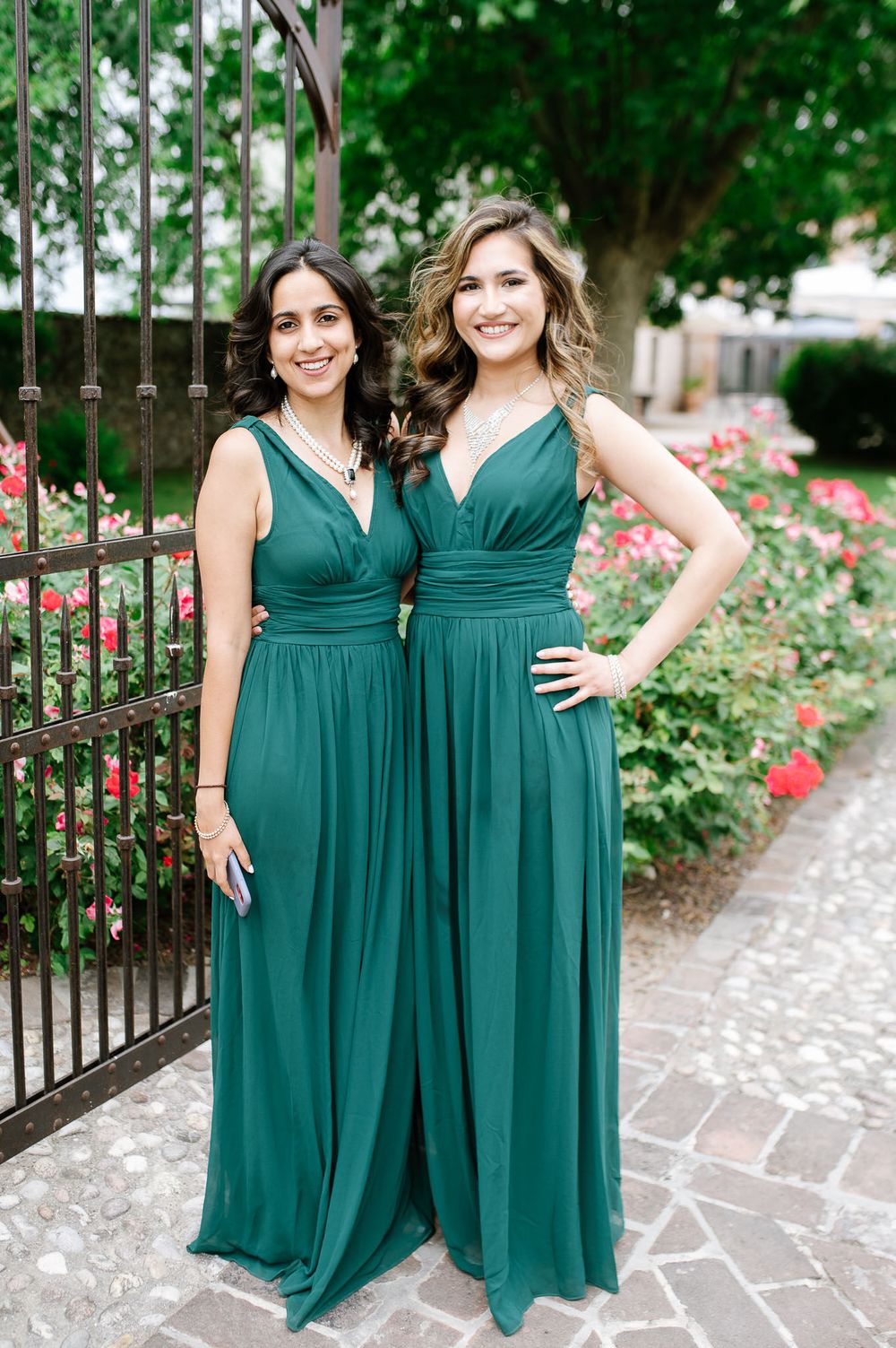 Two women in matching emerald green bridesmaid dresses pose together in a garden setting.