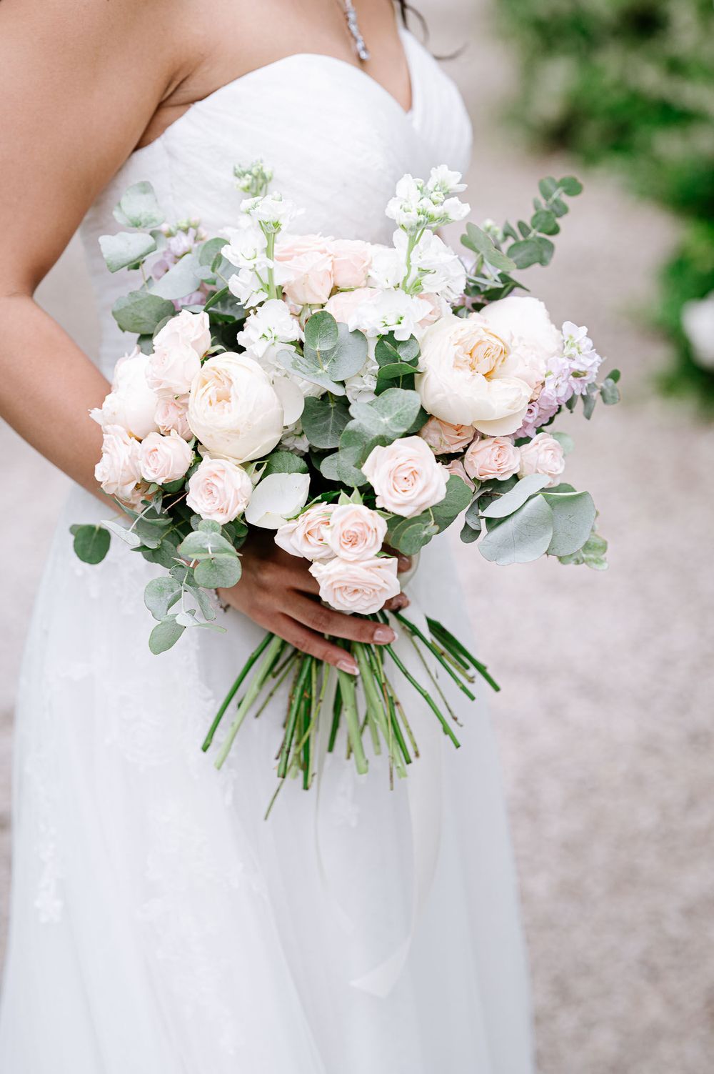 Elegant bridal bouquet with blush roses and eucalyptus held against a white wedding dress.