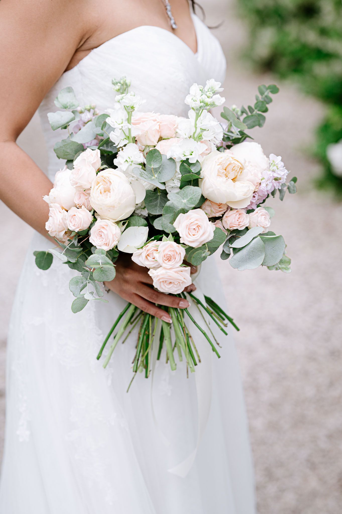 Elegant bridal bouquet with blush roses and eucalyptus held against a white wedding dress.