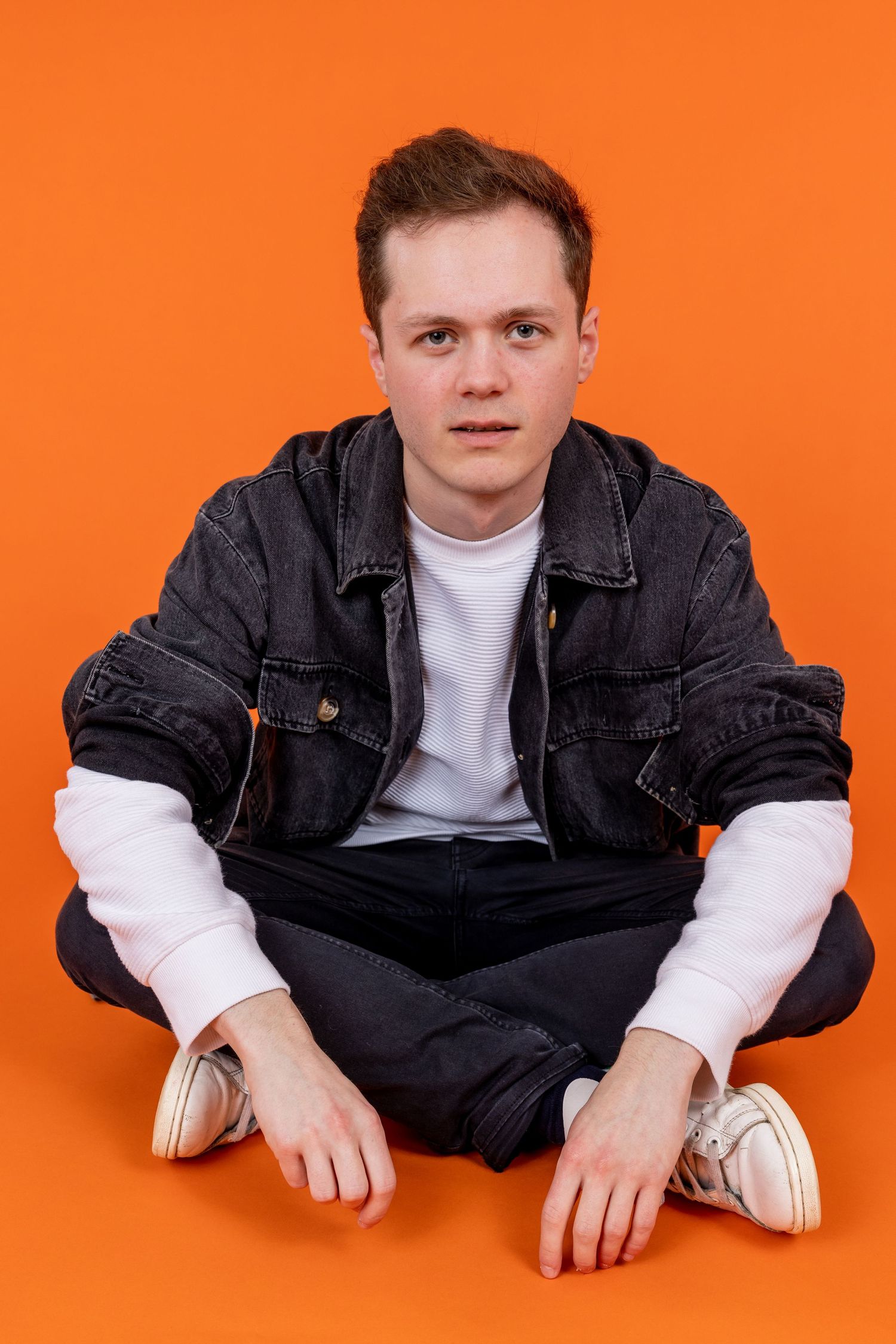 Comedian Oli Court shot in Amy Davies photography in Hove against a bright orange background.