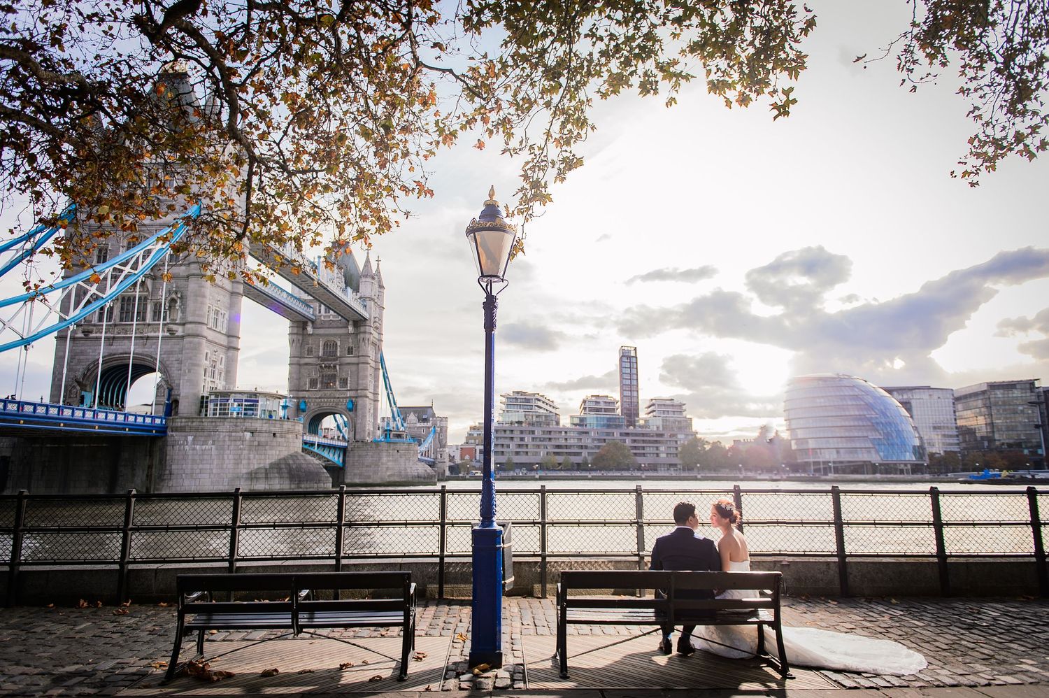 Pre-wedding couple sit quietly on a bench by Tower Bridge