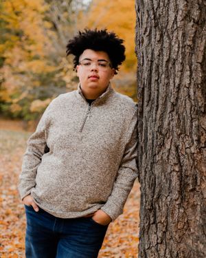 Autumn portrait session featuring beige sweater against tree trunks and fall colors.