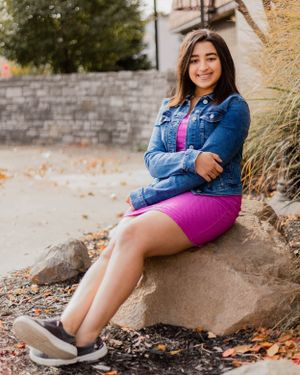 Casual outdoor photoshoot featuring someone sitting on rocks wearing denim and pink.