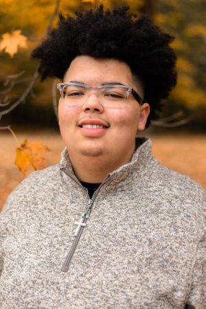 Close-up portrait wearing grey knit sweater with autumn foliage in background.