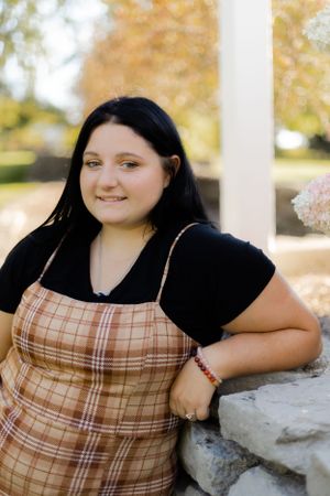 Portrait series against a white column wearing a plaid top and dark shirt.