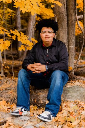Person wearing glasses sits on rock with vibrant yellow fall leaves in background.