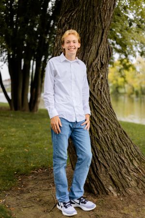 Casual outdoor portrait showing blue jeans and white shirt against a tree trunk in a park setting.