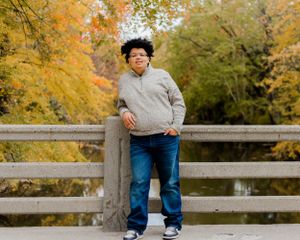 Person in casual attire sits on wooden fence with autumn scenery behind.