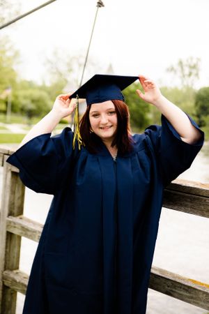 Celebratory graduation poses in navy cap and gown on a wooden deck.