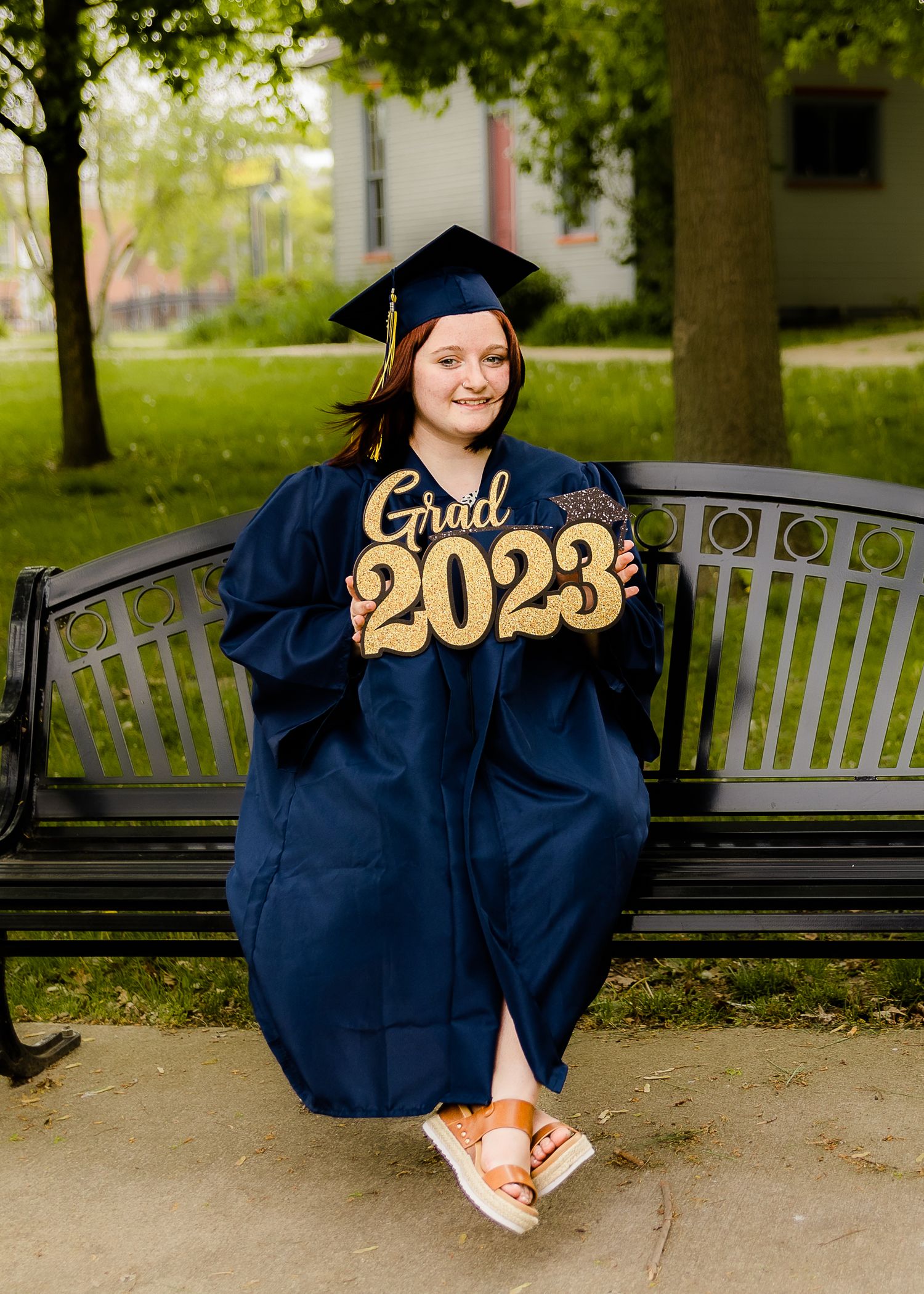 Graduation photos on a park bench wearing a navy cap and gown with gold 2023 text.
