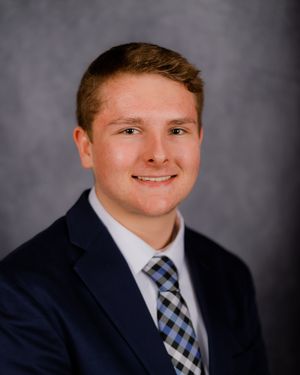 Smiling portrait in formal attire against studio backdrop.