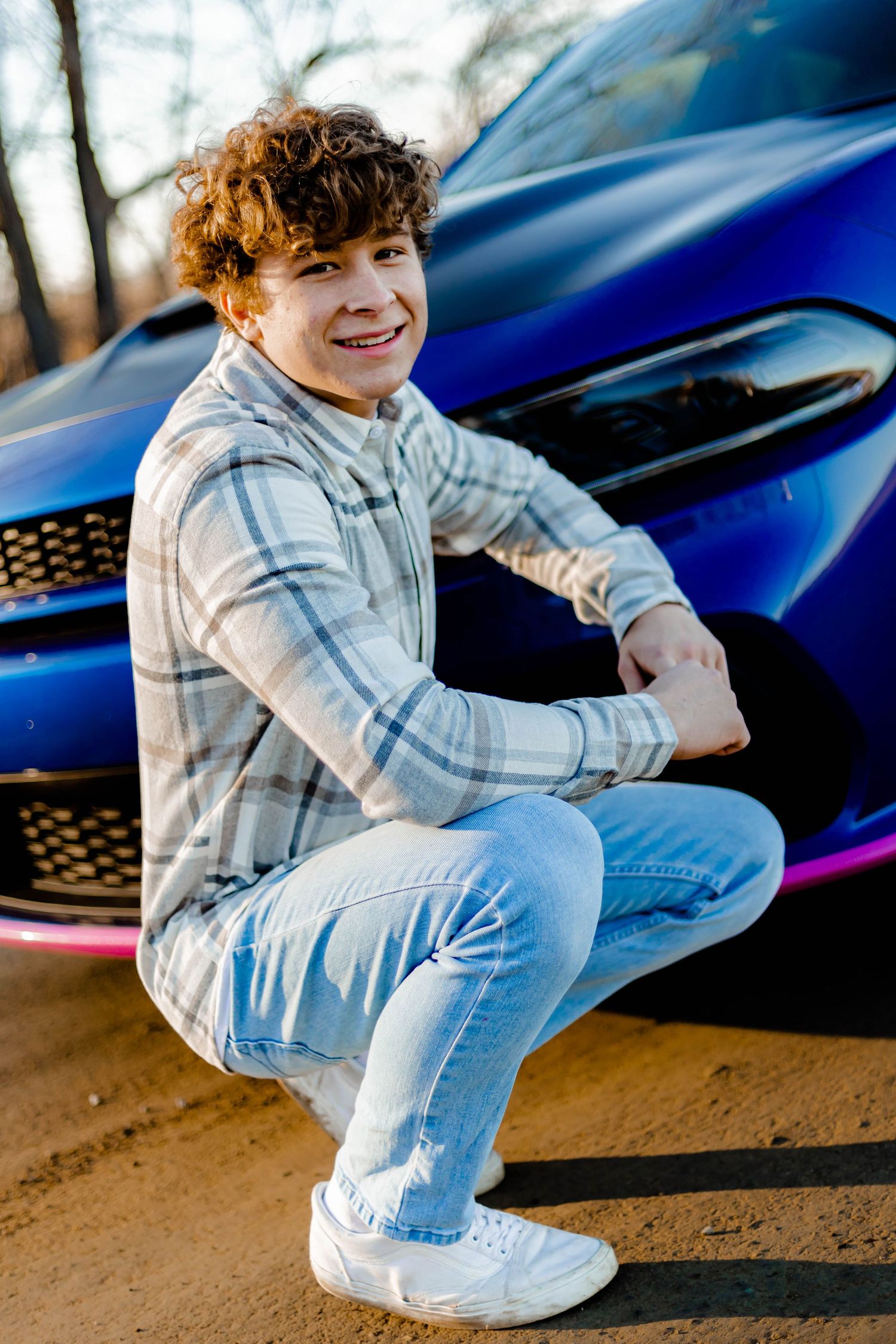 Person crouching next to a blue sports car in casual attire.
