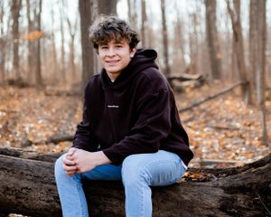 Casual portrait on fallen log in autumn forest wearing dark hoodie.