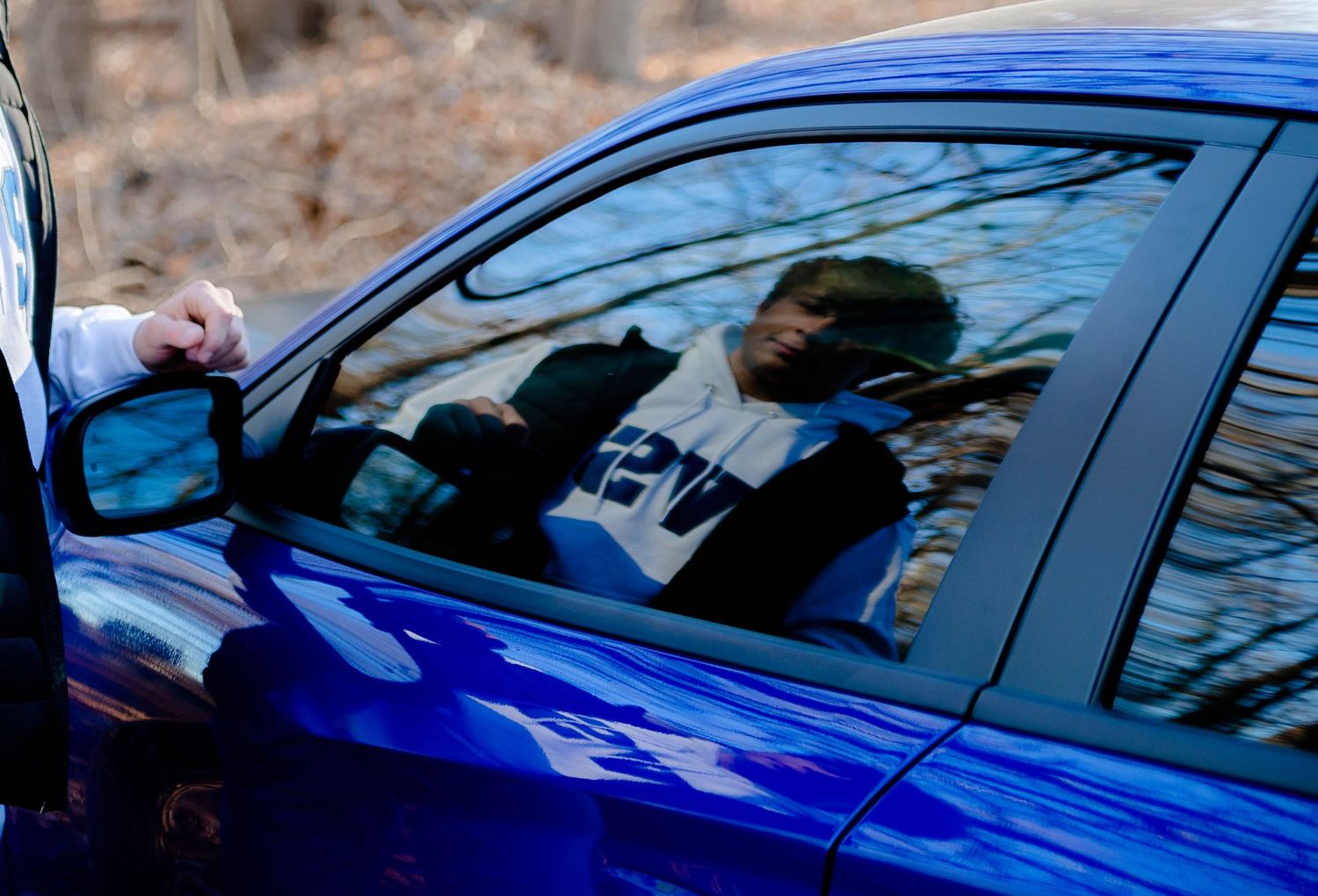 Reflection in window of blue sports car parked in wooded area.