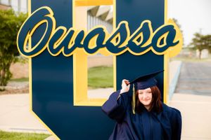 Multiple poses with decorative navy and gold university signage during graduation photoshoot.