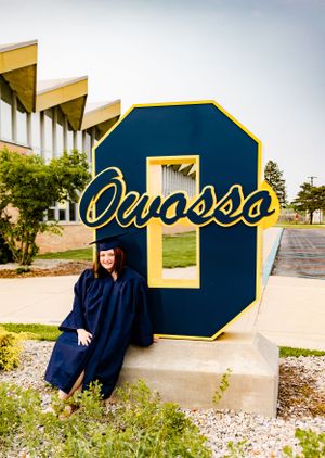 Graduation photos taken in front of large blue and gold university sign.
