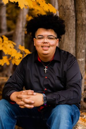 Portrait session in autumn forest with warm golden lighting and black shirt against fall foliage.