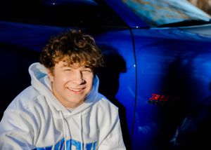 Portrait shot against a bright blue car with winter trees in background.