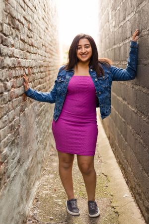 Fashion portrait in an urban alley with brick walls showing casual denim and pink style.
