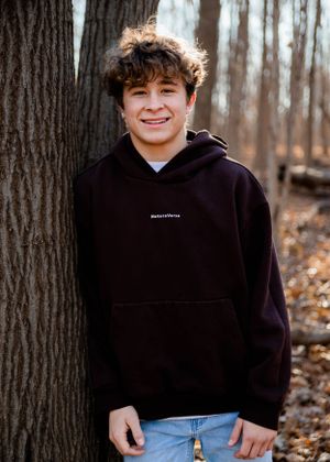Outdoor portrait against tree trunk wearing dark casual clothing.
