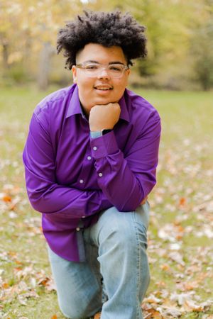 Individual in purple polo shirt poses playfully in field with scattered leaves.