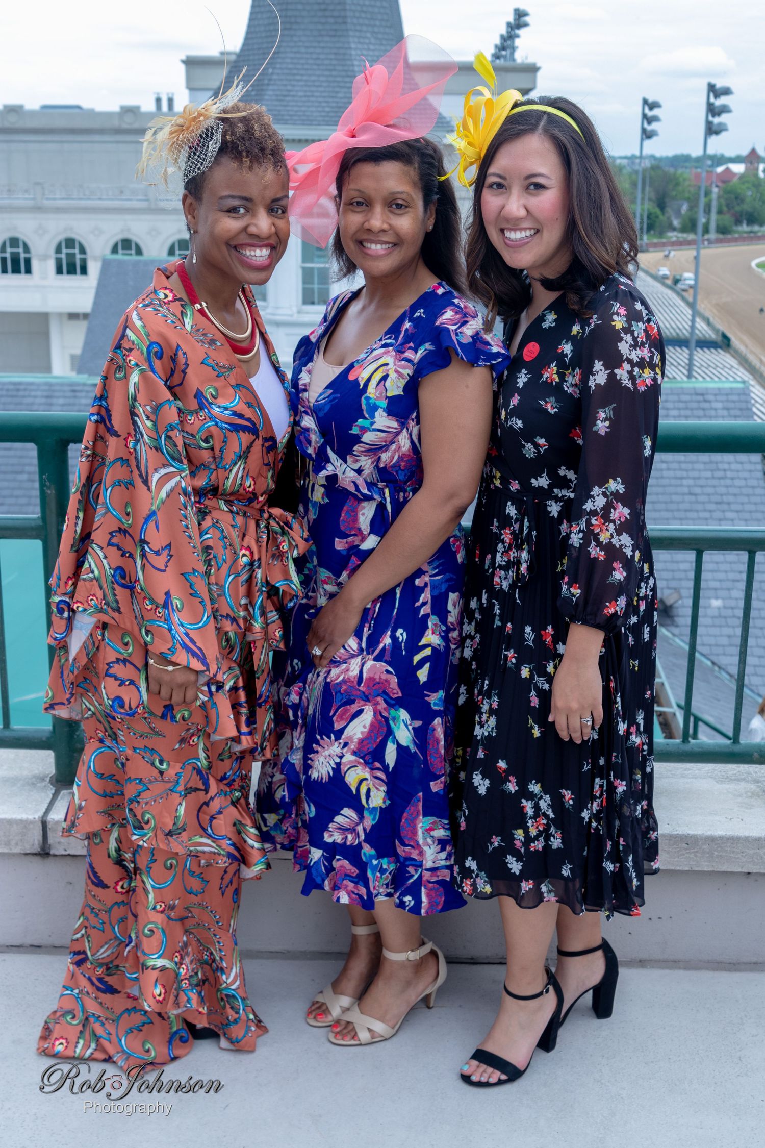 Group in floral dresses posing outdoors with city architecture in background.