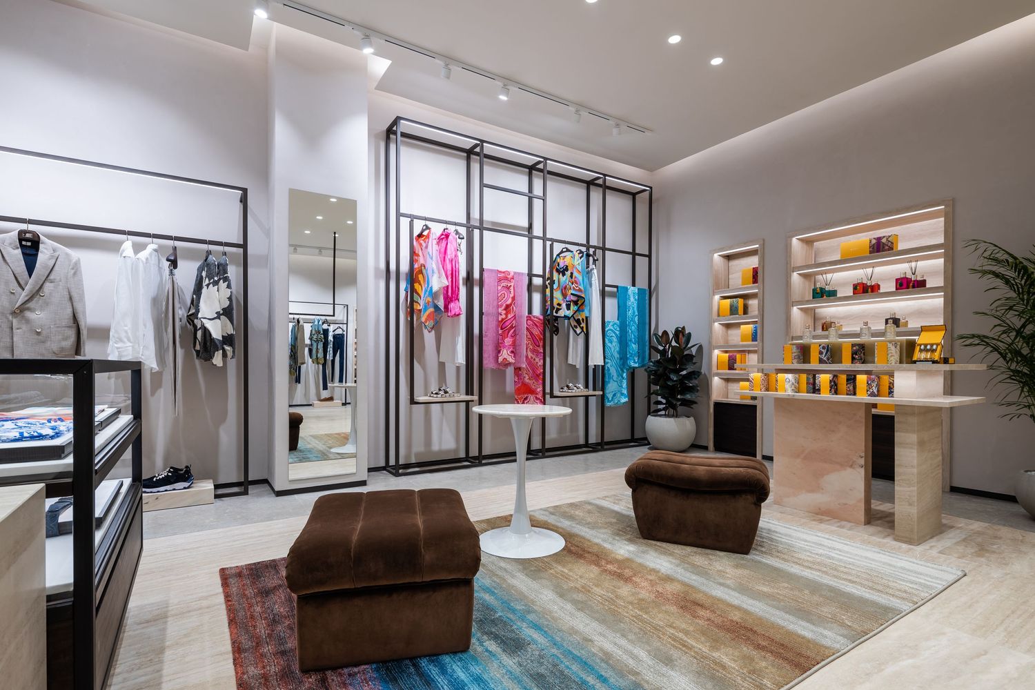 Modern retail boutique interior with colorful clothing displays, brown velvet seating, and a blue patterned rug.