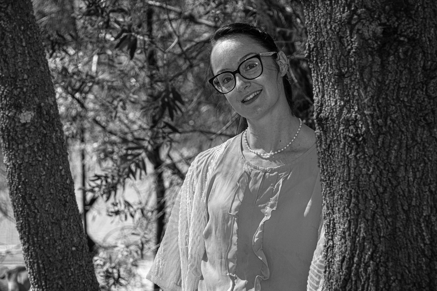 Black and white portrait in dappled sunlight among trees.