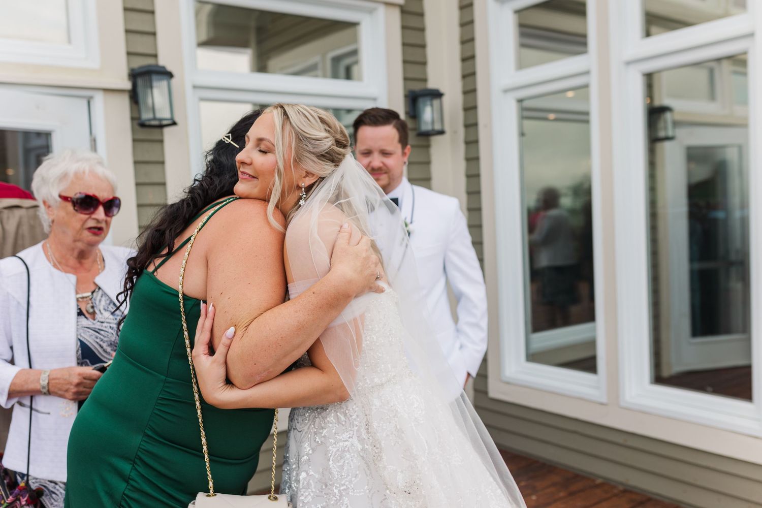 Wedding party celebrating outside classic building with white trim and large windows.