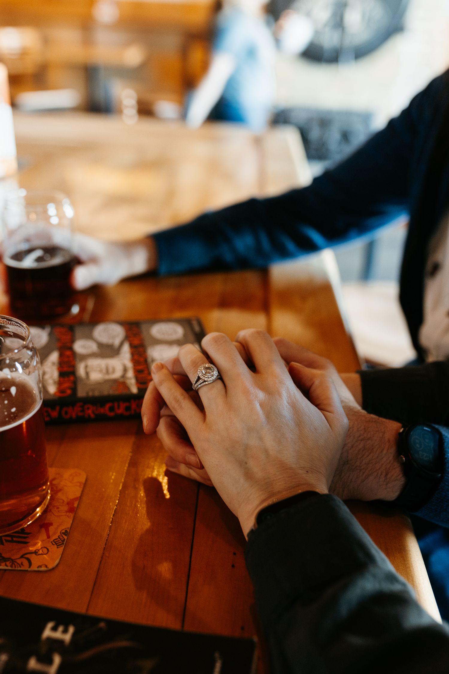 Close-up of hands holding drinks on wooden table with beer coasters.