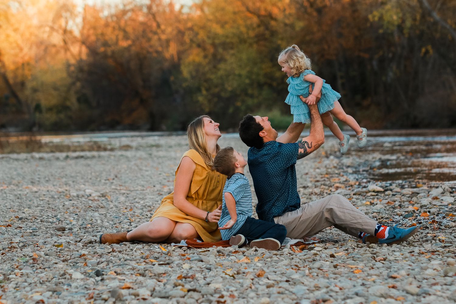 A family relaxes together on a rocky riverbank during golden hour.