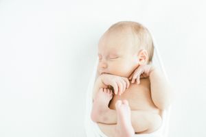 Sleeping newborn baby in peaceful pose against white background with hand near face.