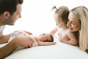 A family shares an intimate moment together on a white surface as they admire their newborn baby.