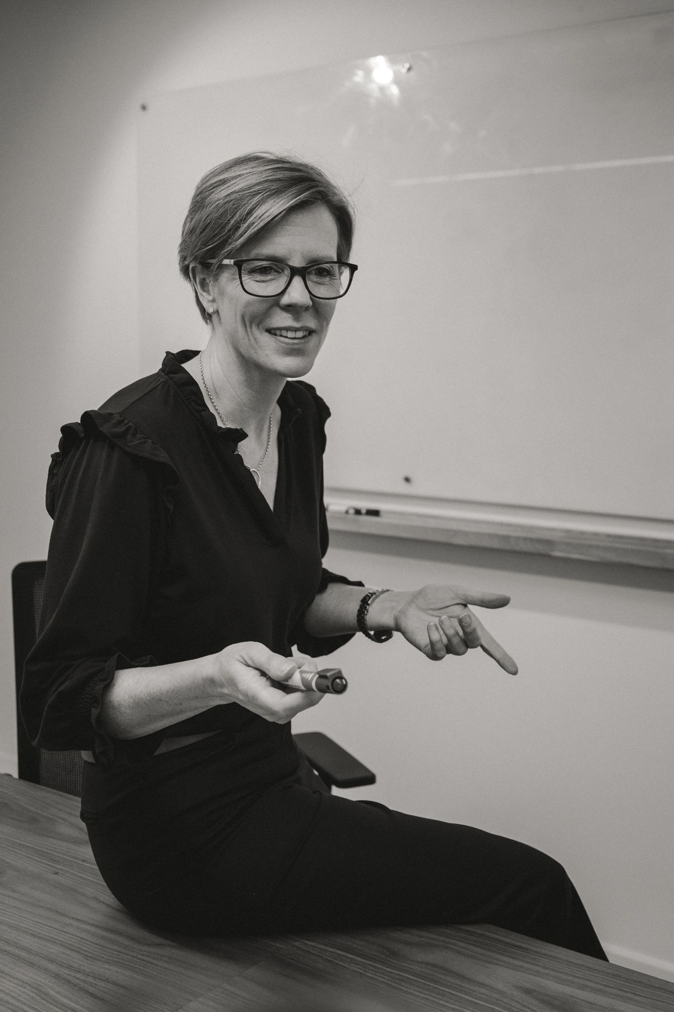 mature woman sitting on the edge of a desk in a board room talking with her hands