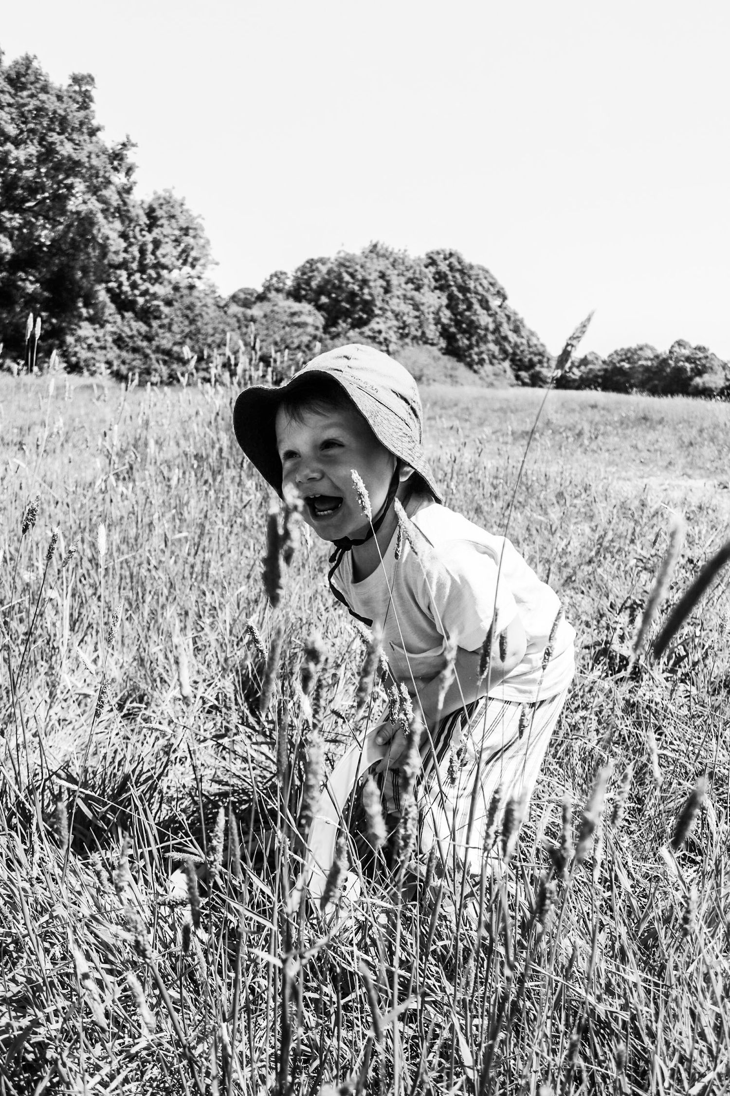 Boy toddler laughing in long grass during Summer in Nonsuch Park, Cheam, Surrey, UK
