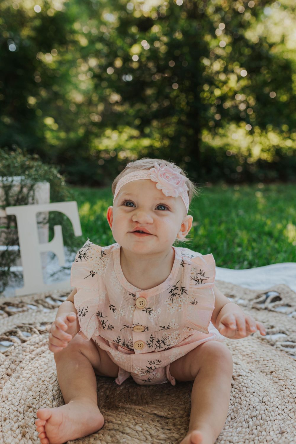 Baby in floral outfit crawls on textured blanket during outdoor photo session.