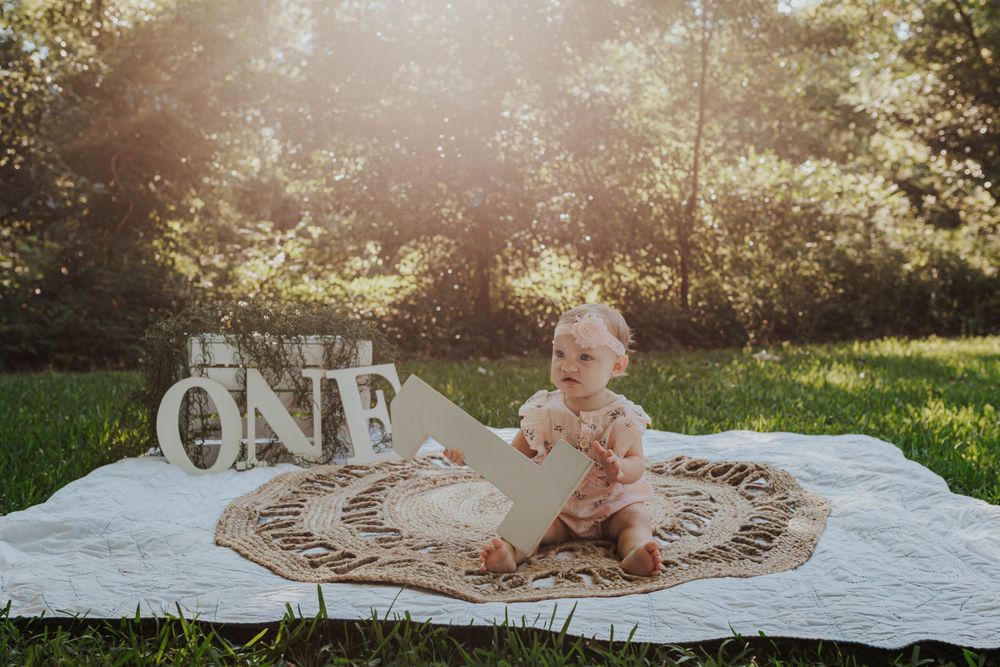 Outdoor cake smash photography session with decorative letters and natural sunlight.