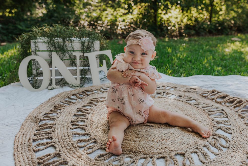Baby crawls on circular jute rug during outdoor first birthday photo session.