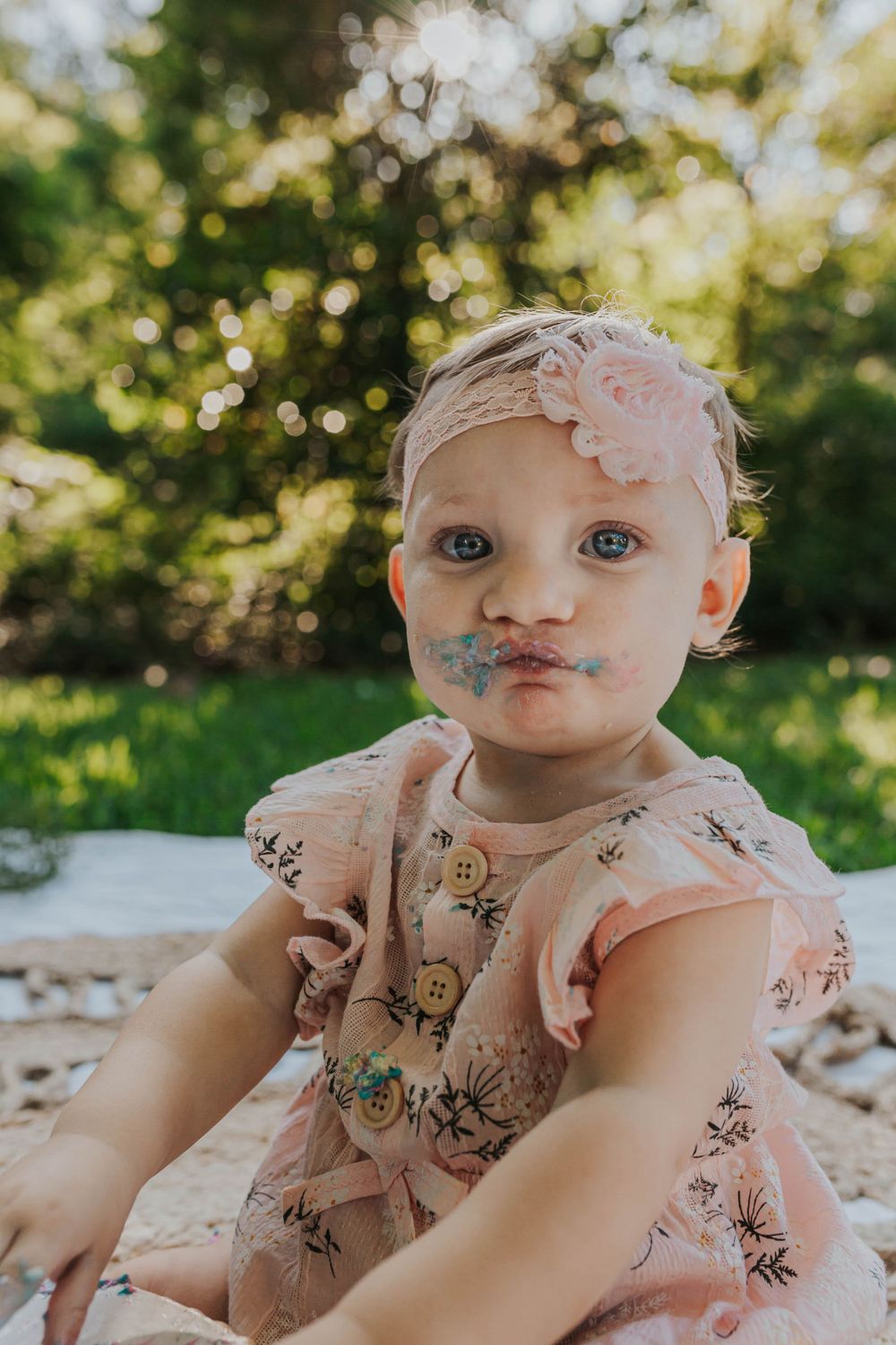 Baby in floral dress poses during outdoor first birthday photo session.