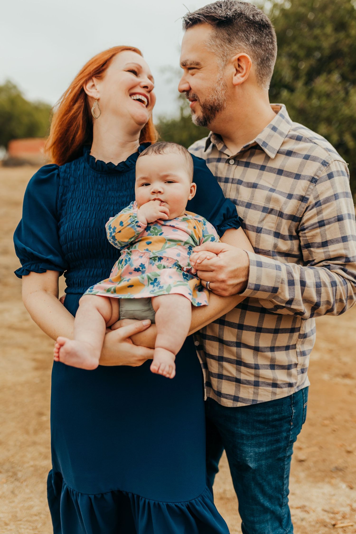 Family of 3 smiles together wearing fall colors during San Diego photo session at Rancho Guajome Adobe in Vista, CA.
