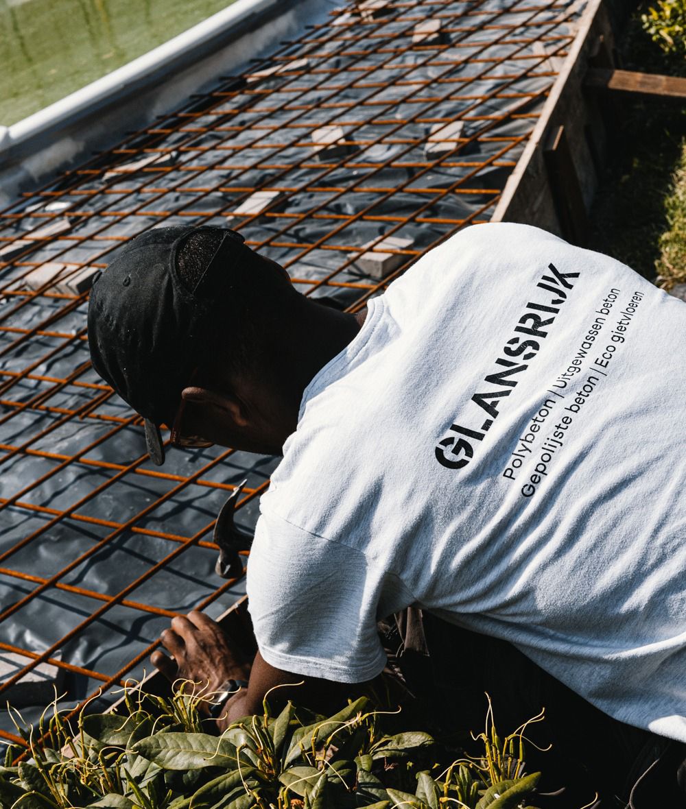 Construction worker in white t-shirt installing metal rebar grid on ground.