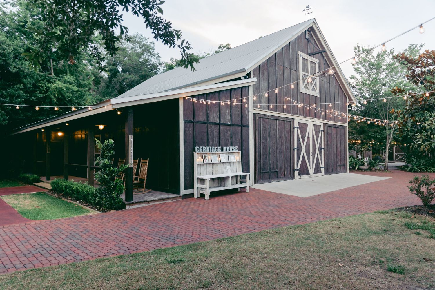 Rustic barn wedding venue exterior with brick pathway and string lights creating a romantic atmosphere.