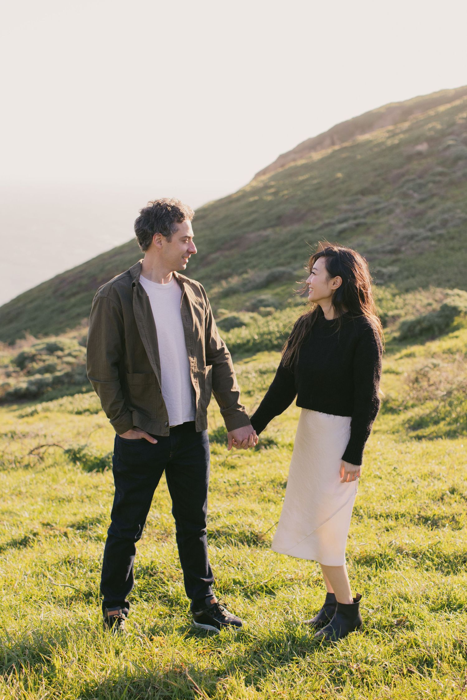 Playful interaction between couple on a grassy coastal hillside during golden hour.