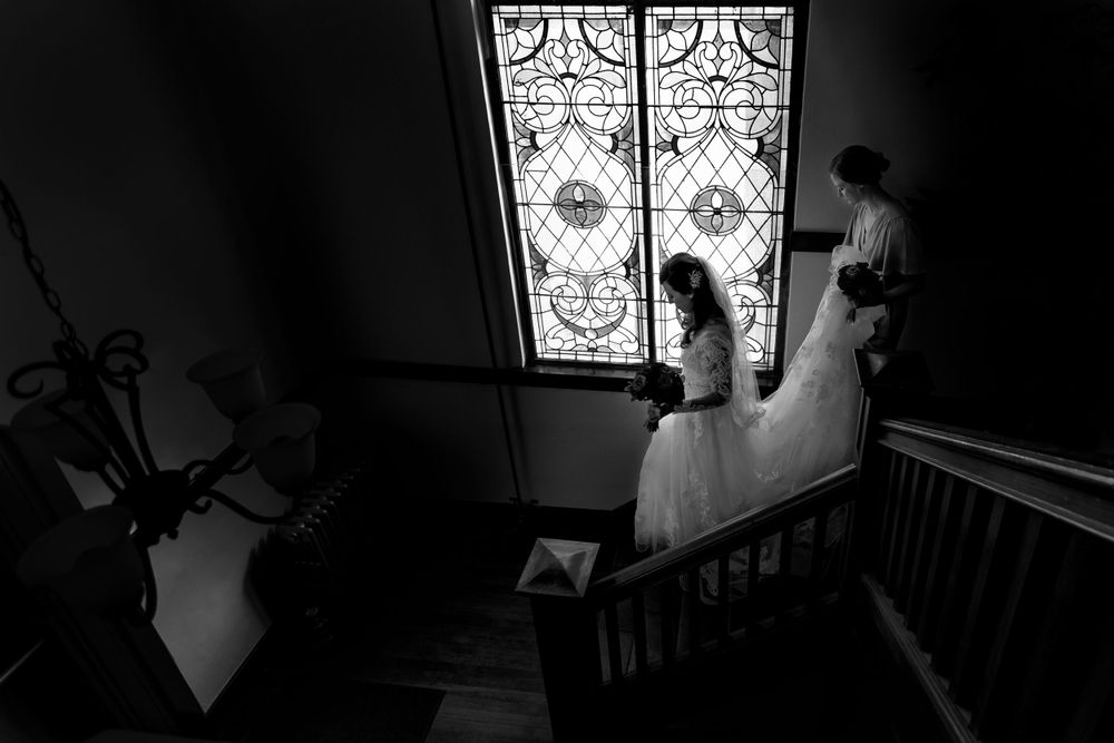 Black and white view looking down an elegant staircase with an ornate stained glass window.