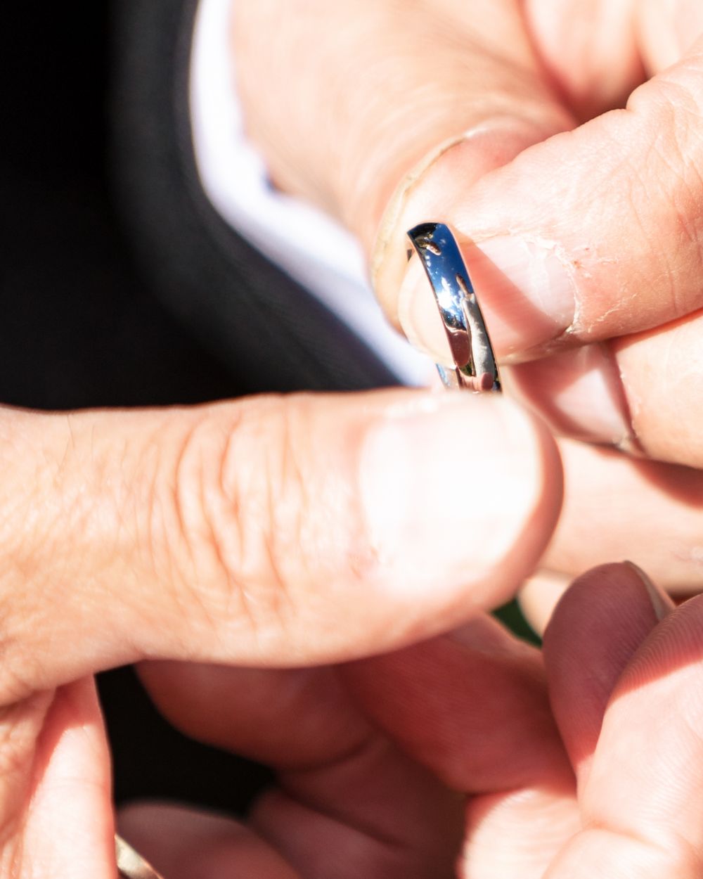 Close-up of hands holding a silver wedding ring with a blue accent.