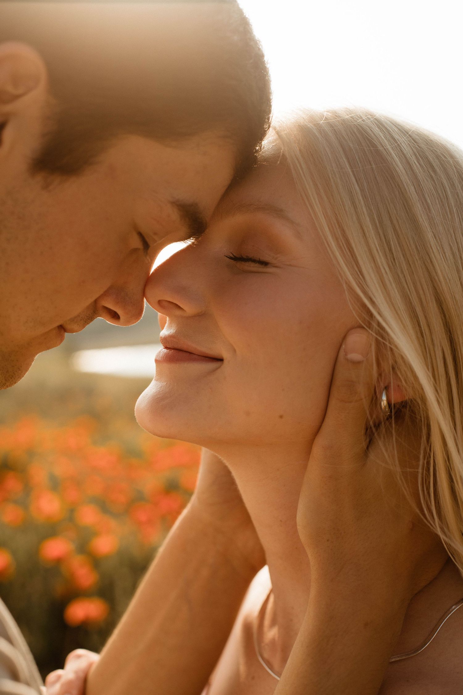 Intimate close-up portrait of couple in warm sunset light among orange wildflowers.