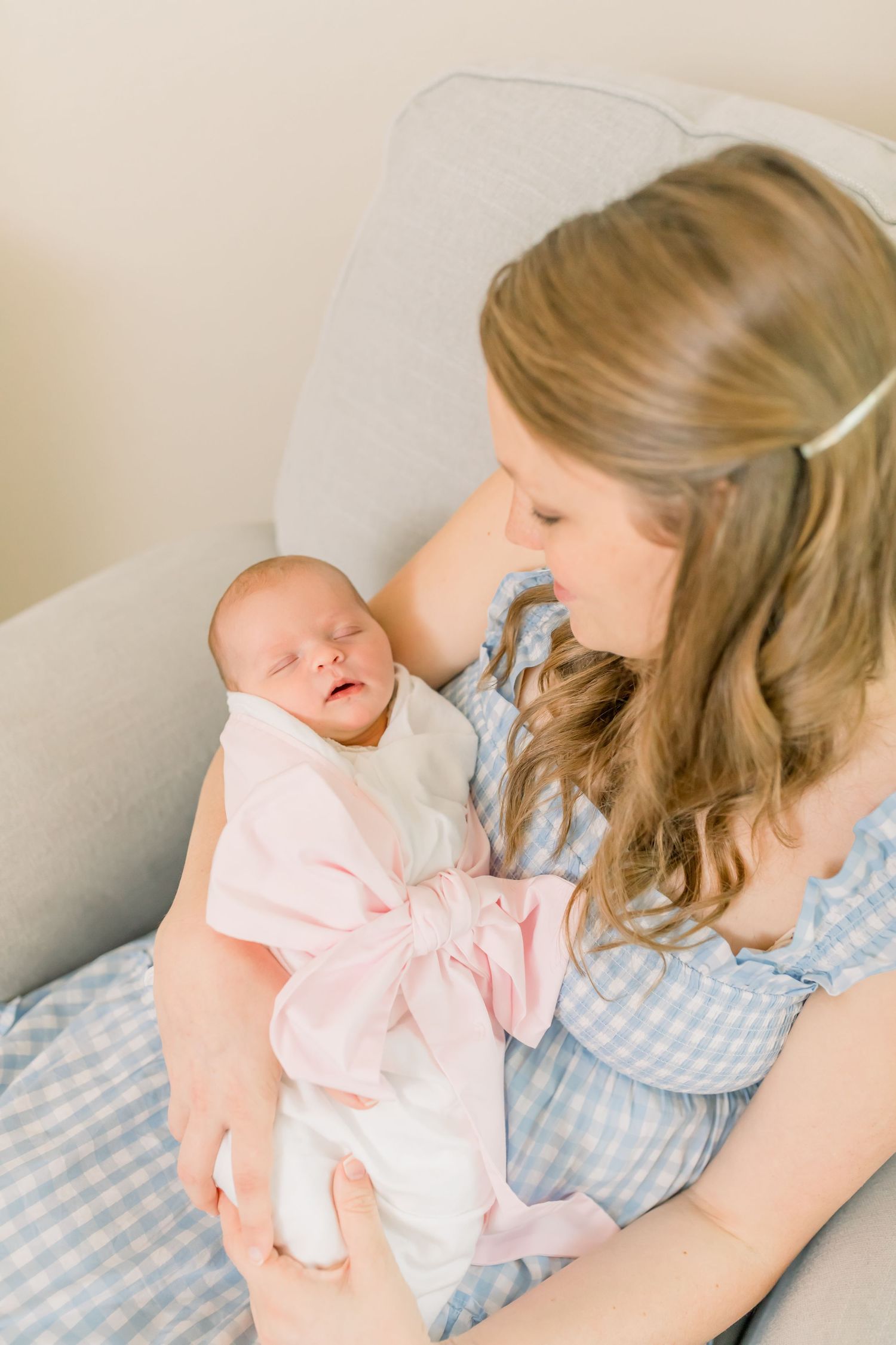 Parent sharing intimate moment with baby in gray armchair.