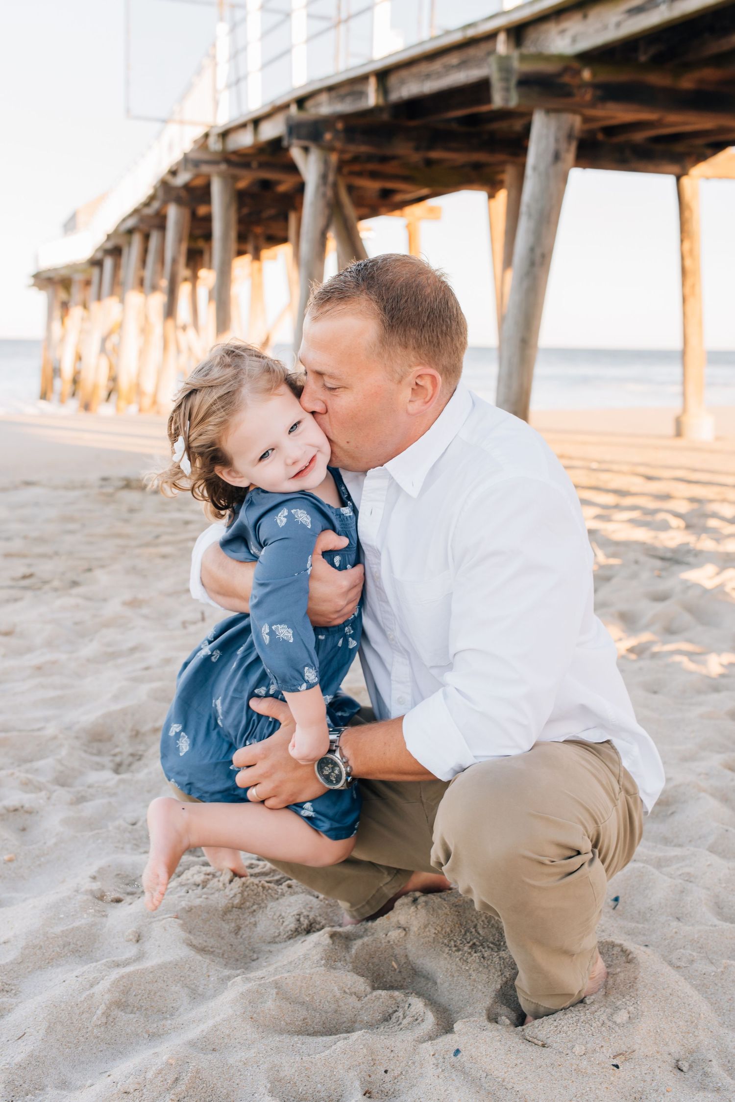 A father squats down to kiss his daughter while Lauren Marie Photography documents this sweet moment.